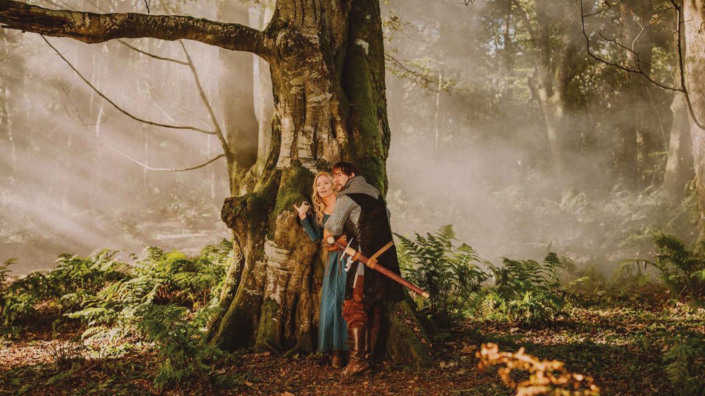 Two actors in medieval costumes pressed up against a tree